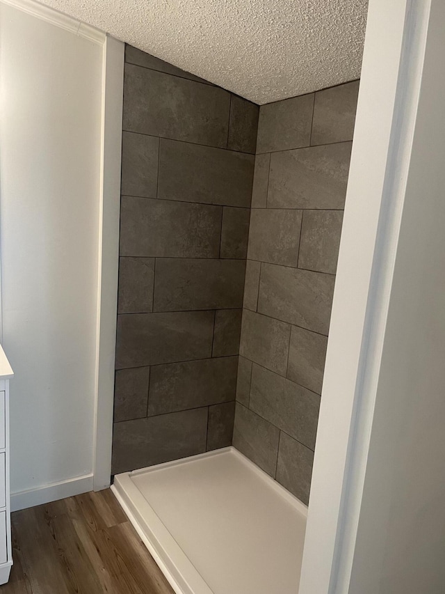 bathroom featuring tiled shower, wood finished floors, baseboards, and a textured ceiling