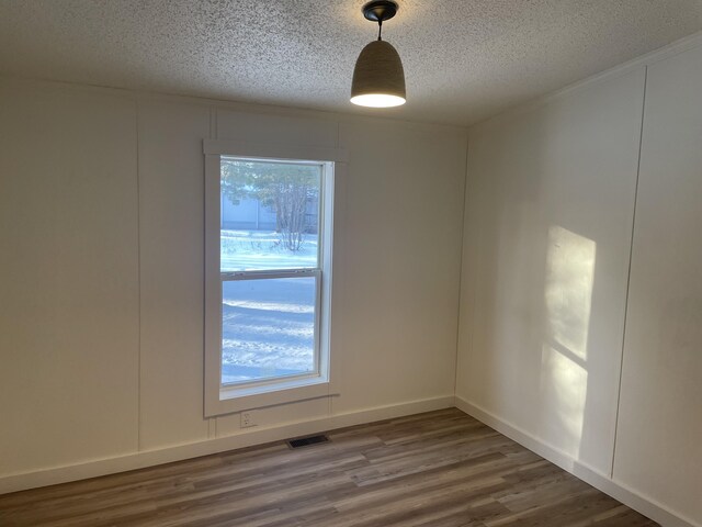 unfurnished room featuring baseboards, wood finished floors, visible vents, and a textured ceiling