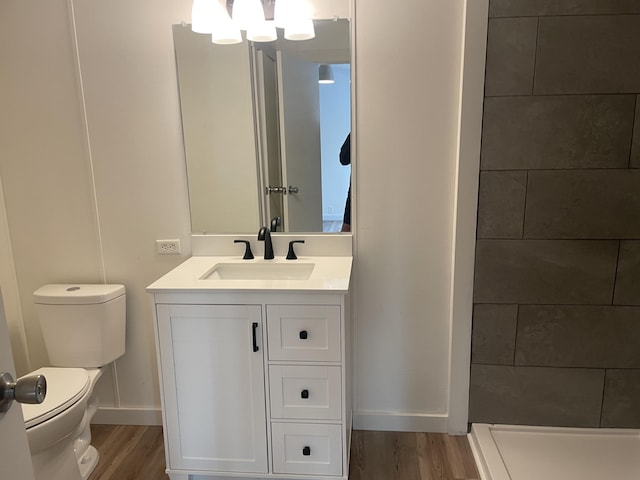 full bathroom with tiled shower, toilet, wood finished floors, and vanity