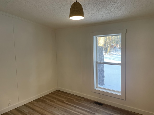 spare room with visible vents, baseboards, a textured ceiling, and wood finished floors