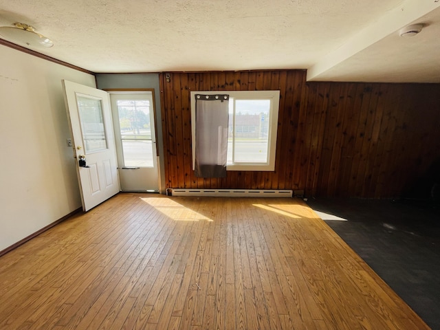 interior space with a baseboard heating unit, a textured ceiling, hardwood / wood-style floors, wood walls, and baseboards