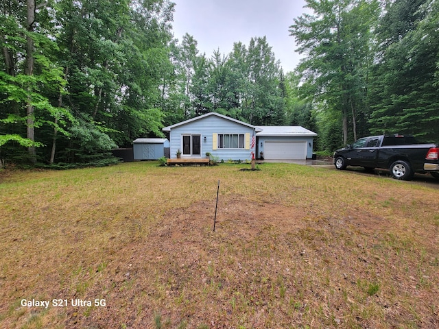 view of front of house featuring an outbuilding, driveway, an attached garage, a front lawn, and a storage shed