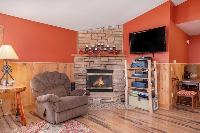 living room featuring wooden walls, a wainscoted wall, lofted ceiling, a stone fireplace, and wood finished floors