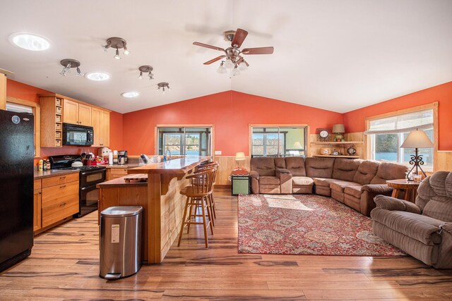 kitchen featuring a breakfast bar area, light wood-style floors, black appliances, and open floor plan