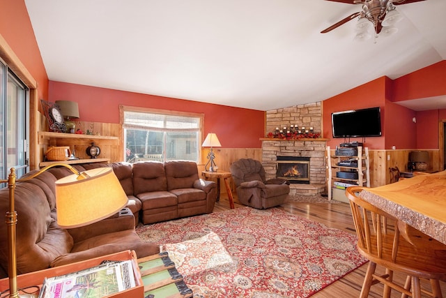 living room with ceiling fan, a wainscoted wall, vaulted ceiling, a fireplace, and wood finished floors