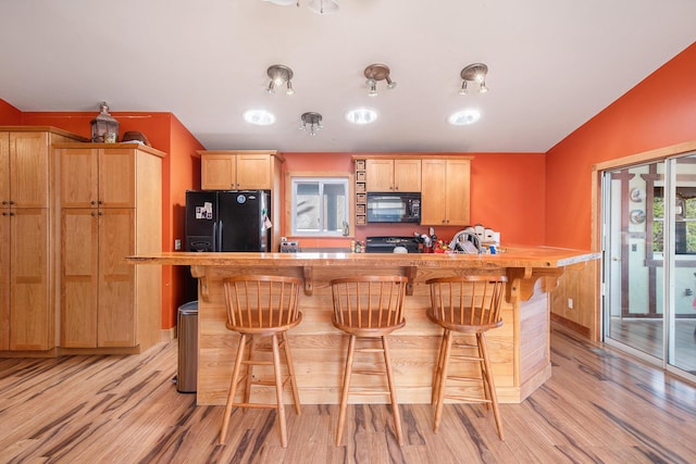 kitchen with light brown cabinetry, black appliances, light countertops, a kitchen breakfast bar, and light wood-type flooring