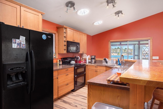 kitchen featuring a kitchen bar, black appliances, light brown cabinetry, a peninsula, and vaulted ceiling