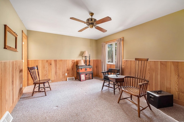 sitting room with a wainscoted wall, a ceiling fan, visible vents, and wood walls