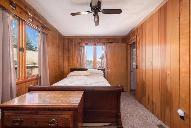 bedroom featuring a ceiling fan, wooden walls, access to exterior, and carpet flooring