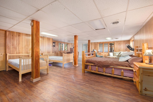 bedroom featuring a drop ceiling, wood finished floors, visible vents, and wood walls