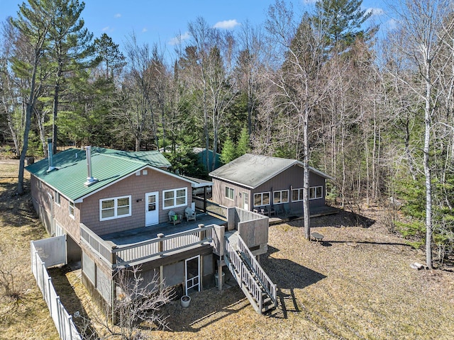 back of property with fence, a forest view, metal roof, a wooden deck, and stairs