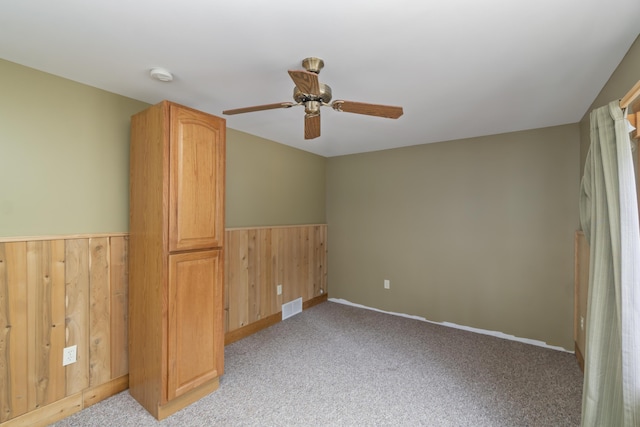 9219 Tall Birch, Gaylord, MI 49735 - unfurnished bedroom featuring a wainscoted wall, light colored carpet, wood walls, ceiling fan, and baseboards