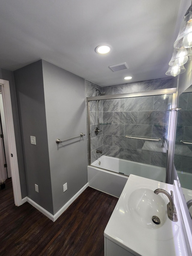 full bathroom featuring visible vents, wood finished floors, shower / bath combination with glass door, baseboards, and vanity