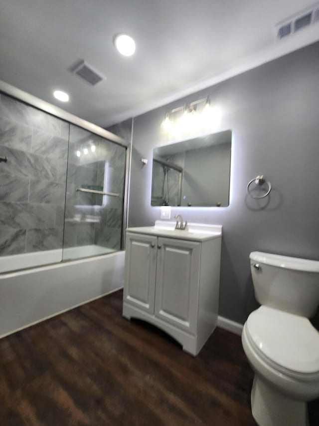 full bath featuring visible vents, toilet, wood finished floors, and bath / shower combo with glass door