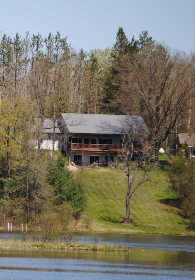 view of front of house featuring a front lawn, a deck with water view, and a wooded view