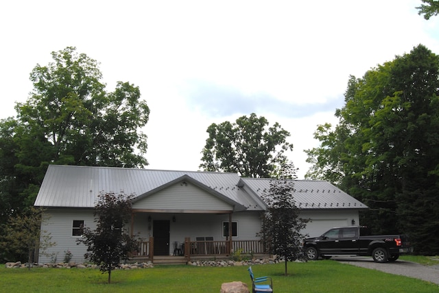 ranch-style house with covered porch, an attached garage, metal roof, and a front lawn