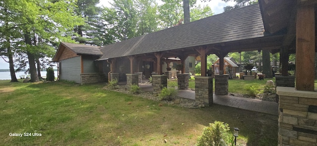 exterior space featuring a shingled roof, a water view, a yard, stone siding, and a patio