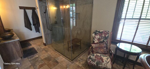 full bath with plenty of natural light, a stall shower, stone finish flooring, and baseboards