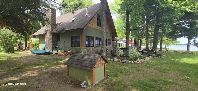 back of house featuring stone siding, a water view, a lawn, and a chimney