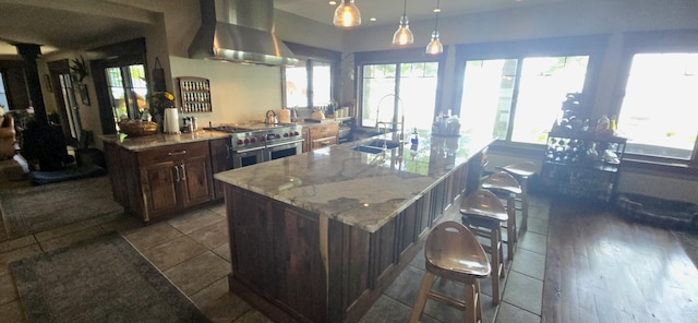 kitchen with a breakfast bar area, double oven range, a sink, a large island, and wall chimney range hood