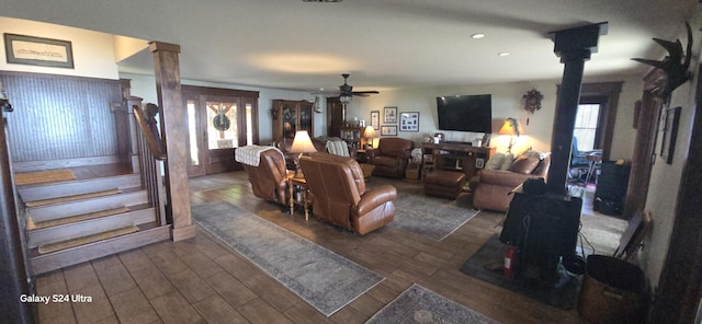 living room featuring ceiling fan, stairs, a wood stove, dark wood-style floors, and ornate columns