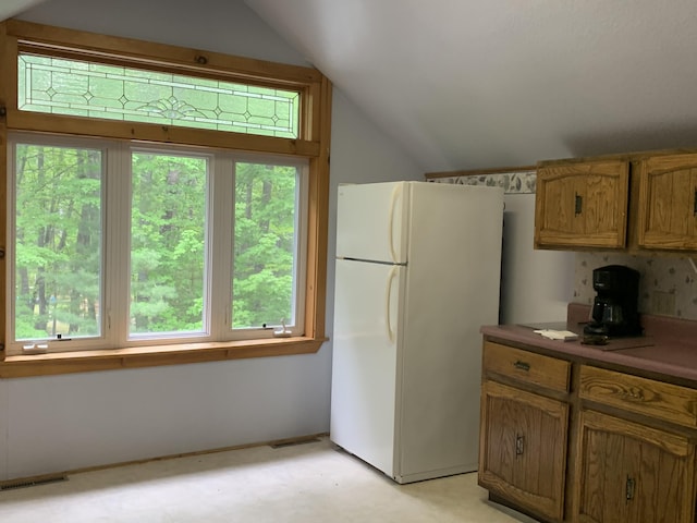 kitchen featuring visible vents, light floors, vaulted ceiling, freestanding refrigerator, and brown cabinetry