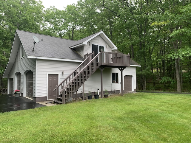 rear view of house featuring a yard, roof with shingles, an attached garage, a wooden deck, and stairs