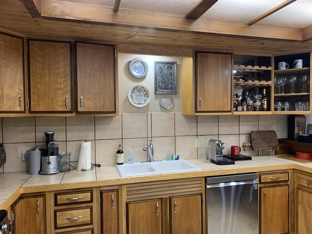 kitchen featuring backsplash, tile countertops, brown cabinets, stainless steel dishwasher, and a sink