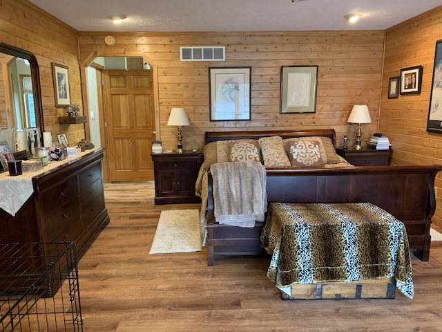 bedroom featuring visible vents, wooden walls, and wood finished floors