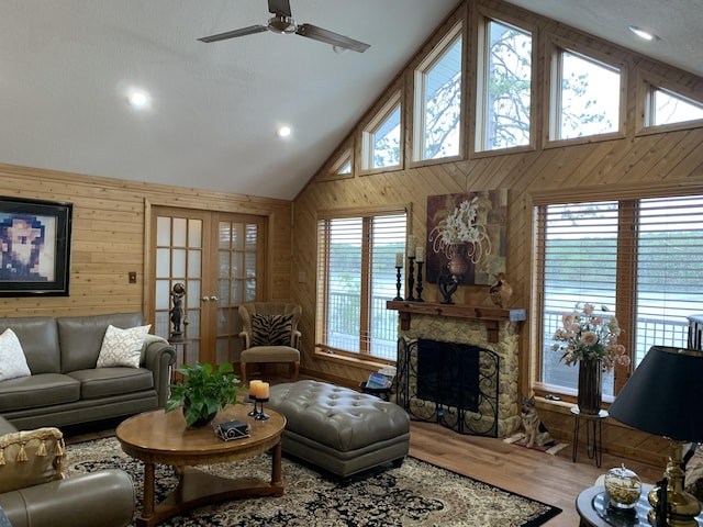 living room featuring wooden walls, a fireplace, wood finished floors, high vaulted ceiling, and a ceiling fan