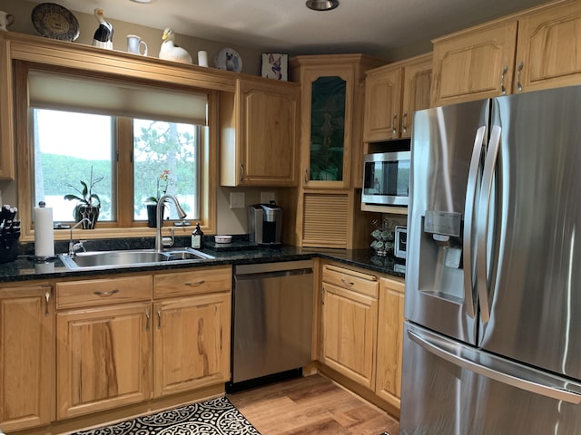 kitchen with glass insert cabinets, dark stone counters, light wood-style flooring, stainless steel appliances, and a sink