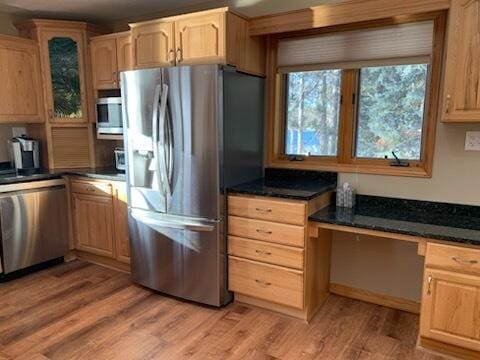 kitchen featuring light brown cabinetry, built in desk, light wood-style flooring, and stainless steel appliances