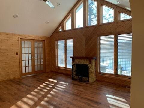 unfurnished living room featuring wooden walls, a fireplace, french doors, wood finished floors, and high vaulted ceiling