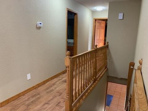 corridor with light wood-type flooring, baseboards, and an upstairs landing