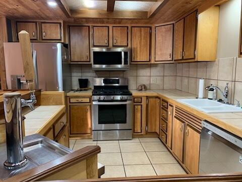 kitchen featuring tile counters, light tile patterned floors, decorative backsplash, stainless steel appliances, and a sink