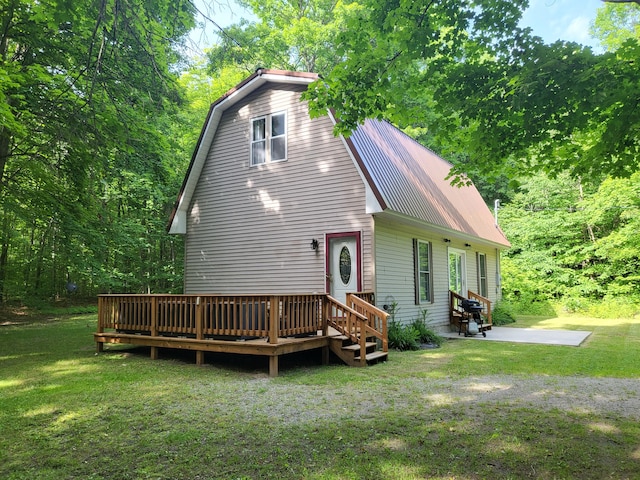 back of house with a gambrel roof, a wooden deck, metal roof, a yard, and a patio