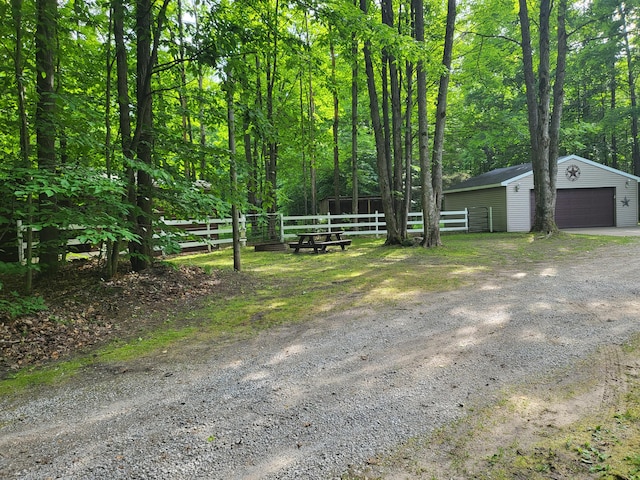 view of yard with a wooded view, a detached garage, an outdoor structure, and fence