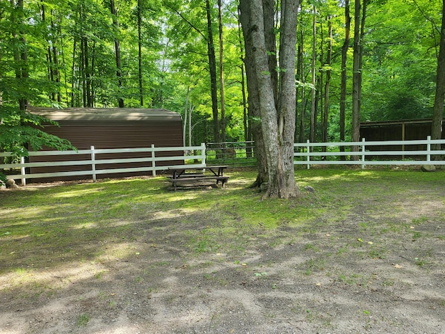 view of yard with a forest view, an outdoor structure, and fence