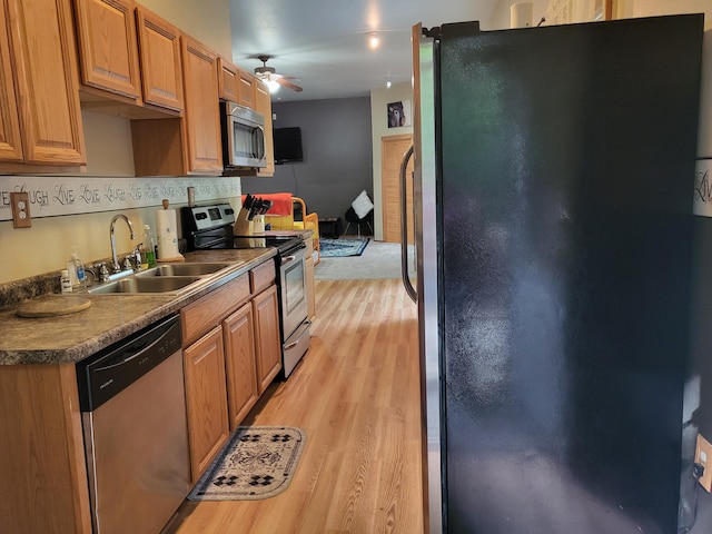 kitchen featuring a ceiling fan, light wood-style flooring, a sink, appliances with stainless steel finishes, and brown cabinets