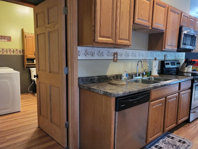 kitchen featuring light wood finished floors, washer / clothes dryer, a sink, stainless steel appliances, and dark countertops