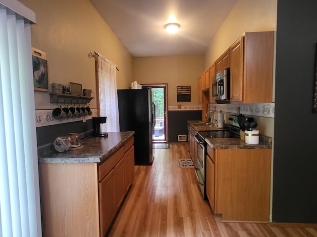 kitchen featuring decorative backsplash, dark countertops, light wood-style flooring, and stainless steel appliances