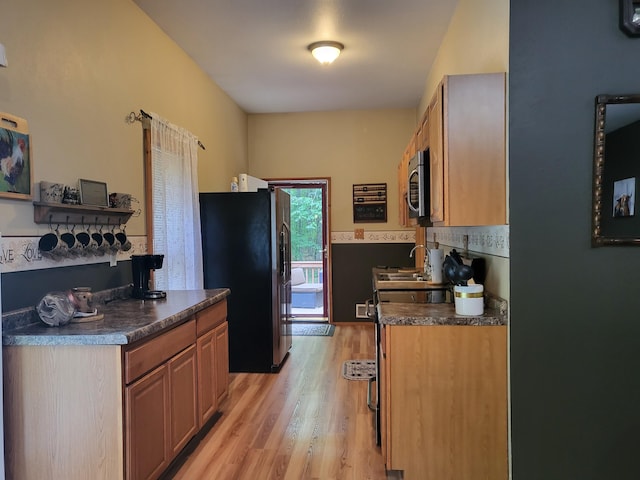 kitchen with dark countertops, appliances with stainless steel finishes, light wood-style floors, and a sink