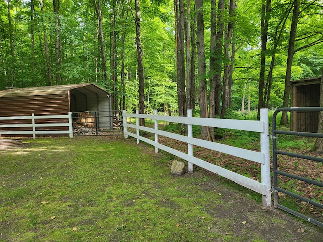 view of yard featuring a carport, a wooded view, and fence