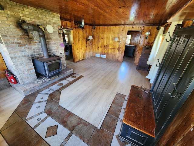 living area with wooden walls, wood finished floors, a wood stove, washer / clothes dryer, and wooden ceiling