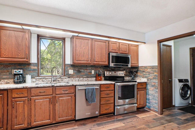 kitchen featuring a sink, washer / clothes dryer, dark wood finished floors, appliances with stainless steel finishes, and brown cabinetry