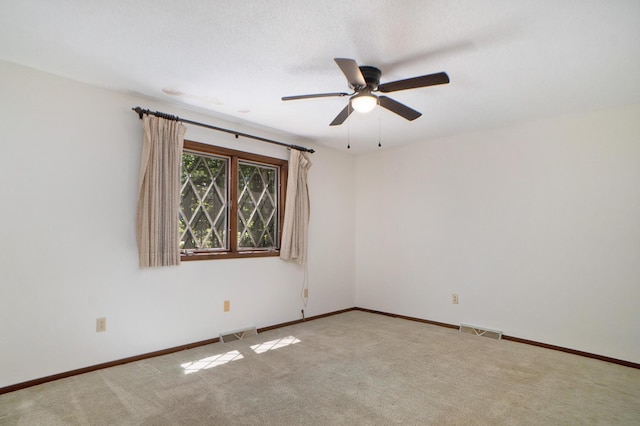 carpeted empty room with baseboards, visible vents, and ceiling fan