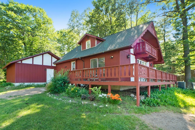 back of property with a lawn, cooling unit, a shingled roof, and a balcony