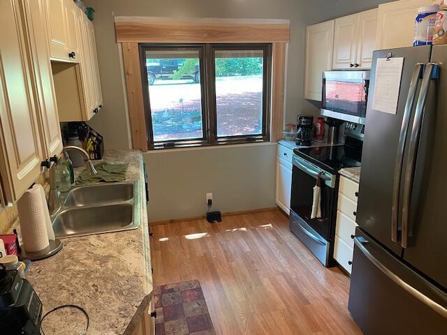 kitchen with electric range, a sink, white cabinetry, freestanding refrigerator, and light wood-style floors