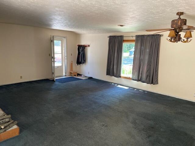 unfurnished room with plenty of natural light, a textured ceiling, ceiling fan, and dark carpet