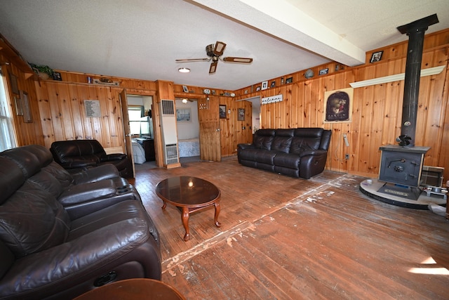 living room featuring beam ceiling, a ceiling fan, hardwood / wood-style flooring, wooden walls, and a wood stove